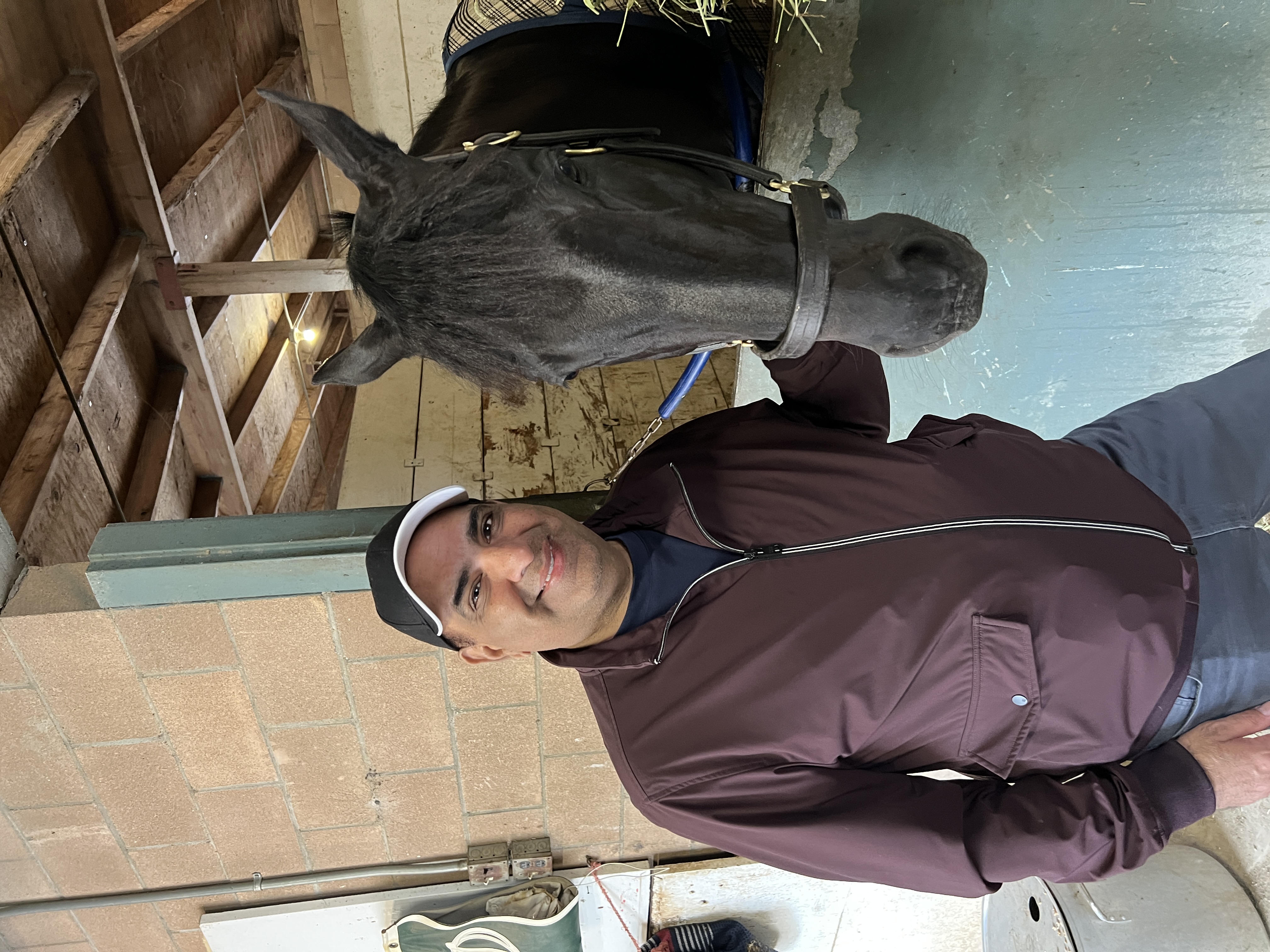 Jeffrey Sengara standing beside a dark horse at the stable